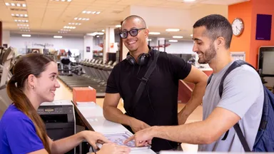 Two men happily chatting with a gym receptionist as she shows them a document