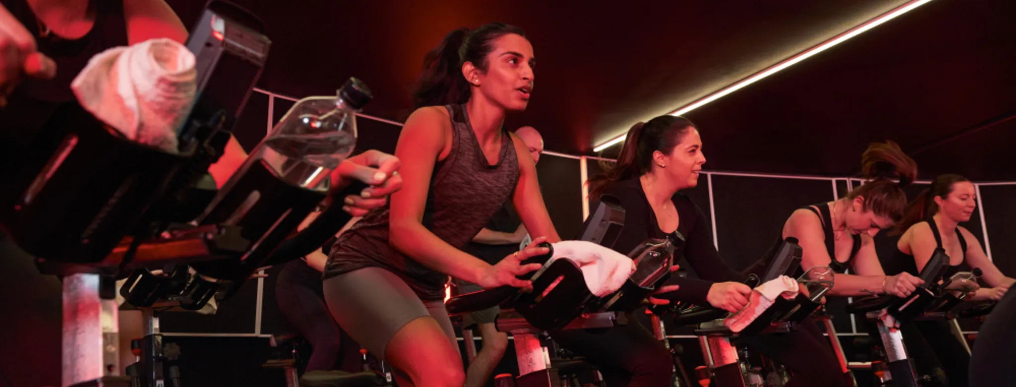 Group fitness class of many people on excercise bikes in room that is lit by red lights