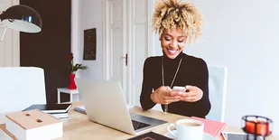Person looking at phone while at desk with laptop