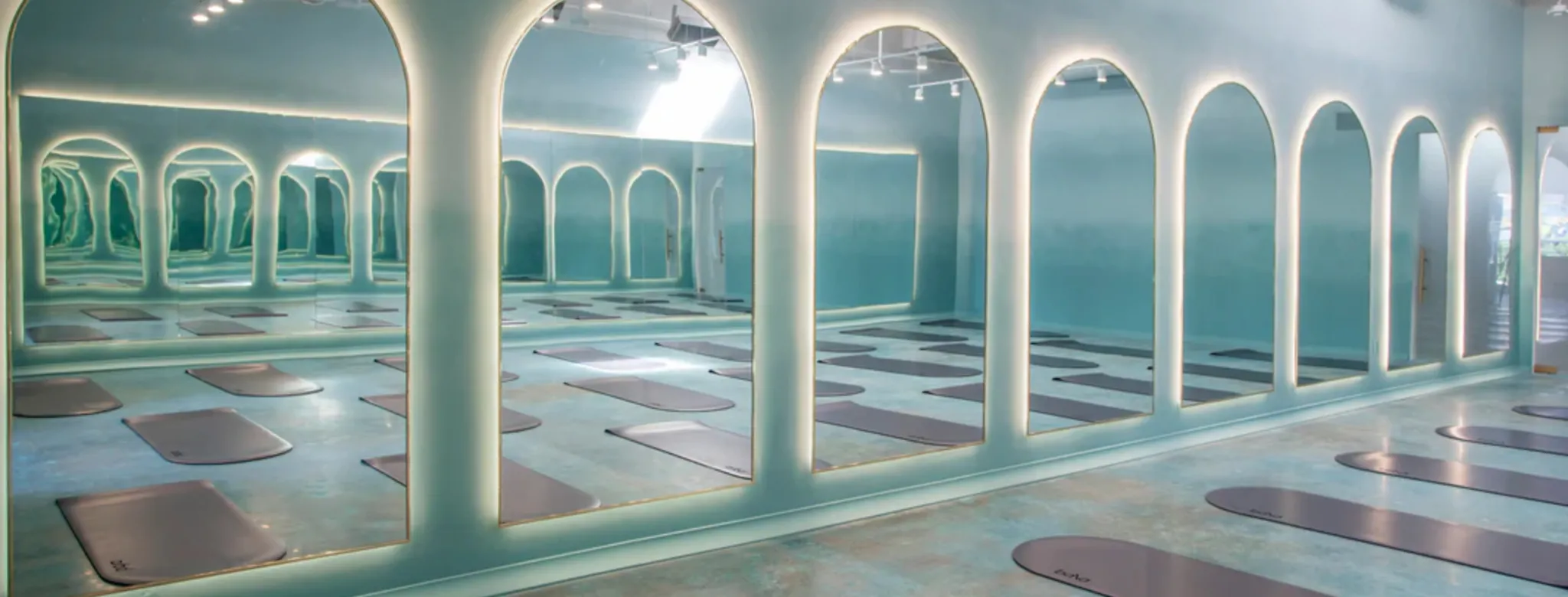 Empty room full of yoga mats with serene blue lighting and high arched floor to ceiling windows.